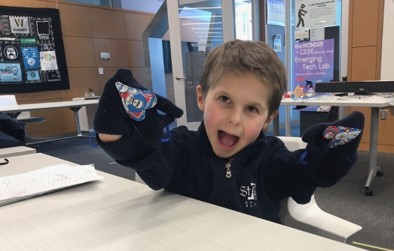 A young boy holds up his hands, which are wearing Star Wars mittens, and his face has a big goofy smile