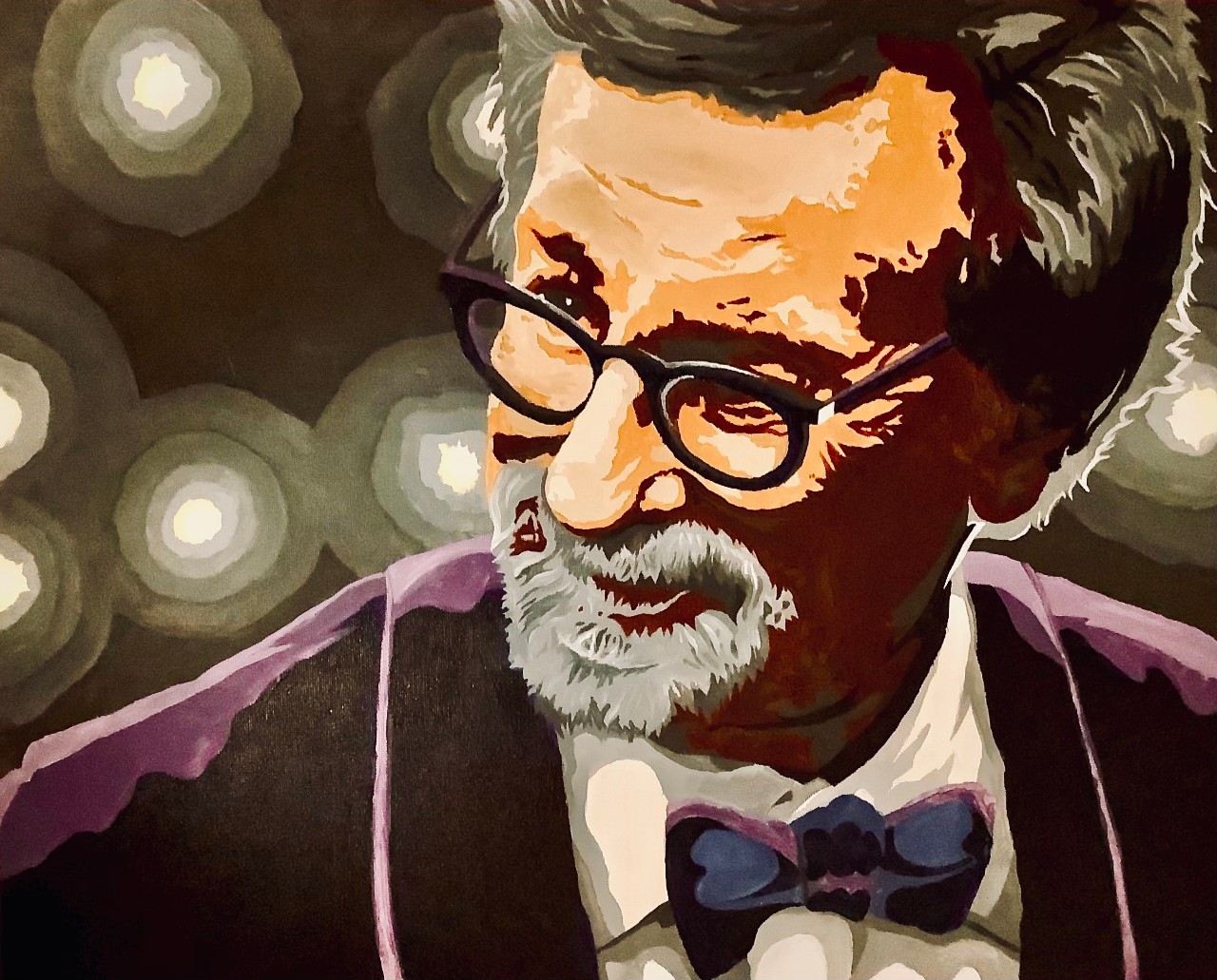 Artwork showing the face of film director Stephen Spielberg. He is shown with his head tiled to the side, looking off to the side. He has short black and gray hair, a gray goatee, black glasses and a purple blazer and bowtie.