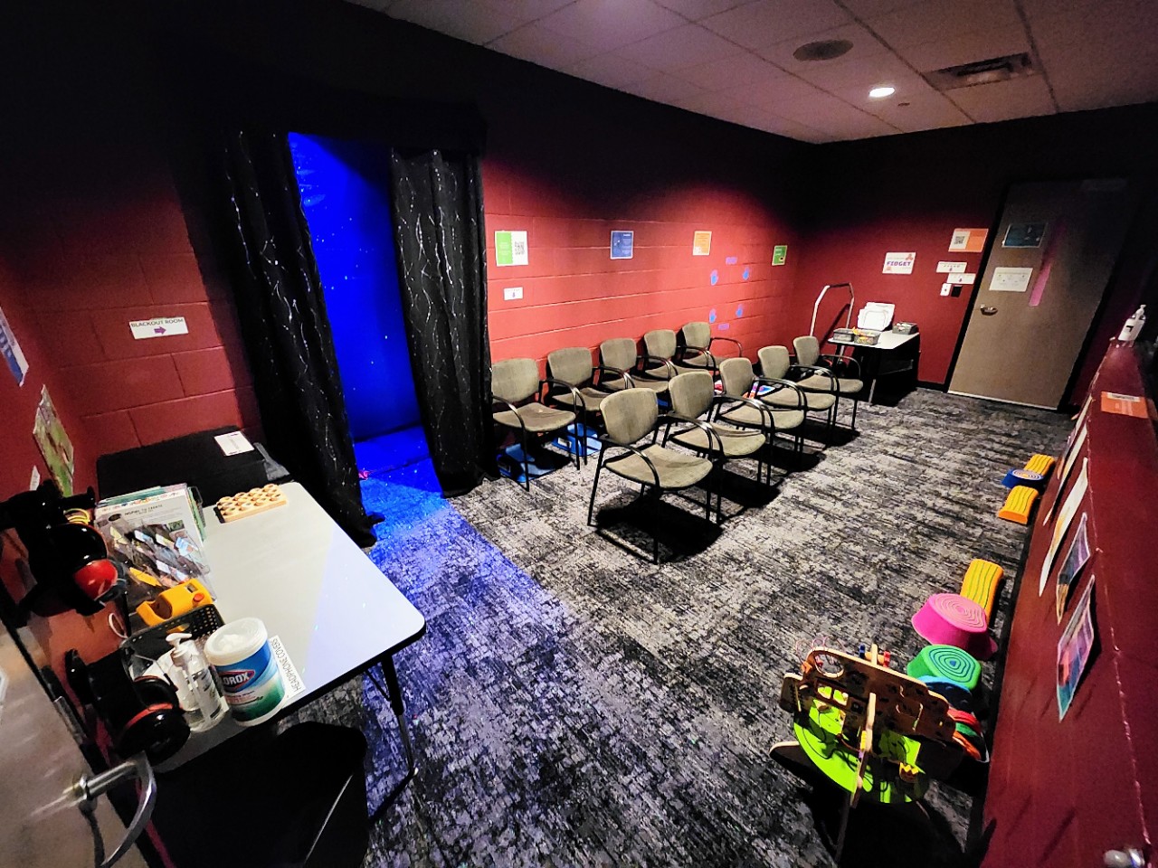 a room with chairs, low lighting, and some colorful toys and a window where attendees can watch the theater stage