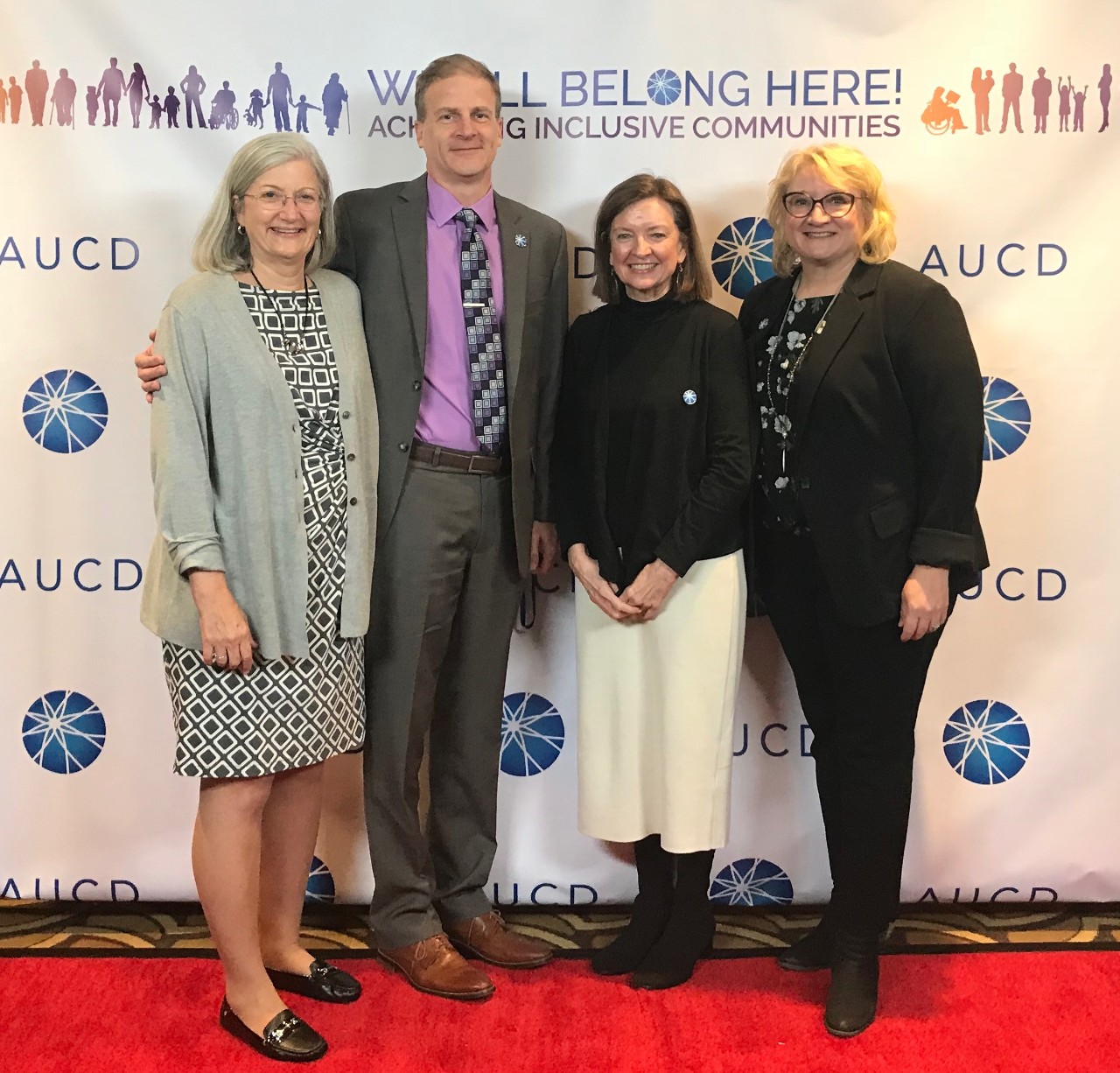The photo shows three women and one man, all professionally dressed, posing at the Association of University Centers on Excellence in Disabilities Conference. 
